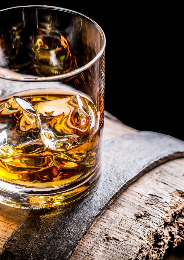 Amber Scotch whisky served over ice in a crystal glass on a wooden table